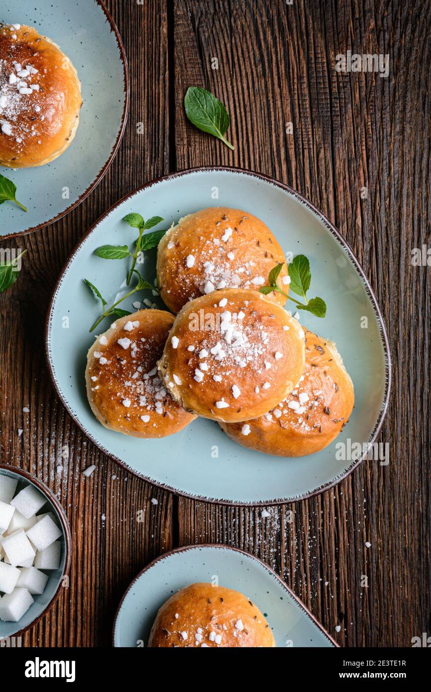 Bollos de baño, pastelería dulce inglesa clásica vidriada con jarabe, rematado con semillas de alcaravea y cubos de azúcar triturados sobre fondo de madera rústica Foto de stock