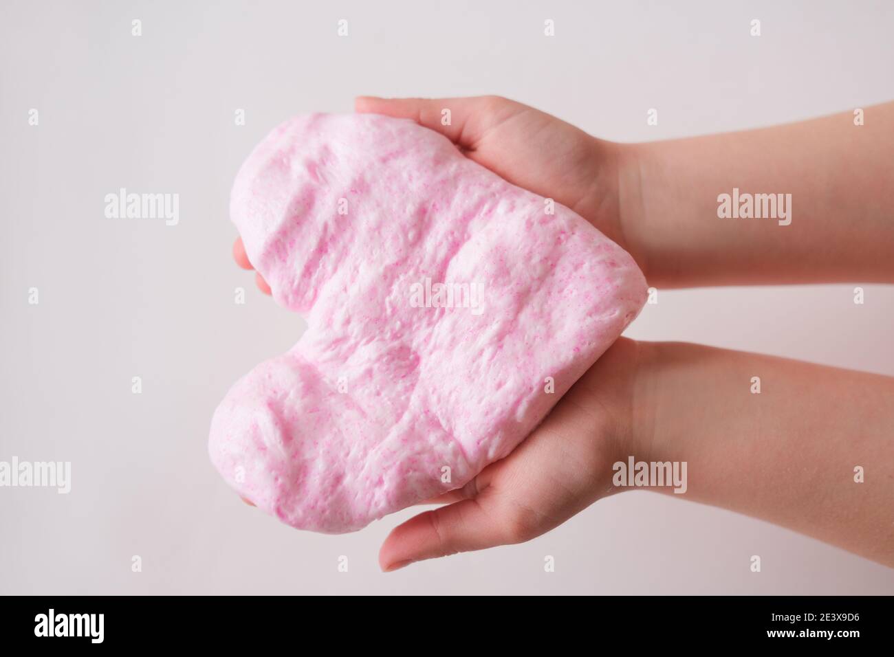 Slime rosa o juguete de goma de manos en manos de los niños. Slime suave en  forma de corazón proyecto de bricolaje. Ocio y juguetes caseros concepto.  Actividades en el interior durante