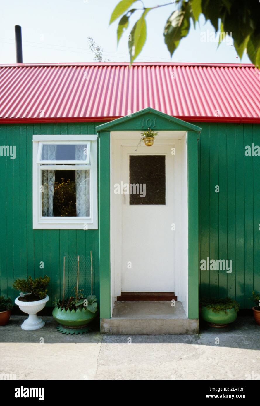 Casa de madera pintada de verde brillante con techo rojo y puertas blancas  con porche. Plantas en macetas fuera, irlanda del Norte Fotografía de stock  - Alamy