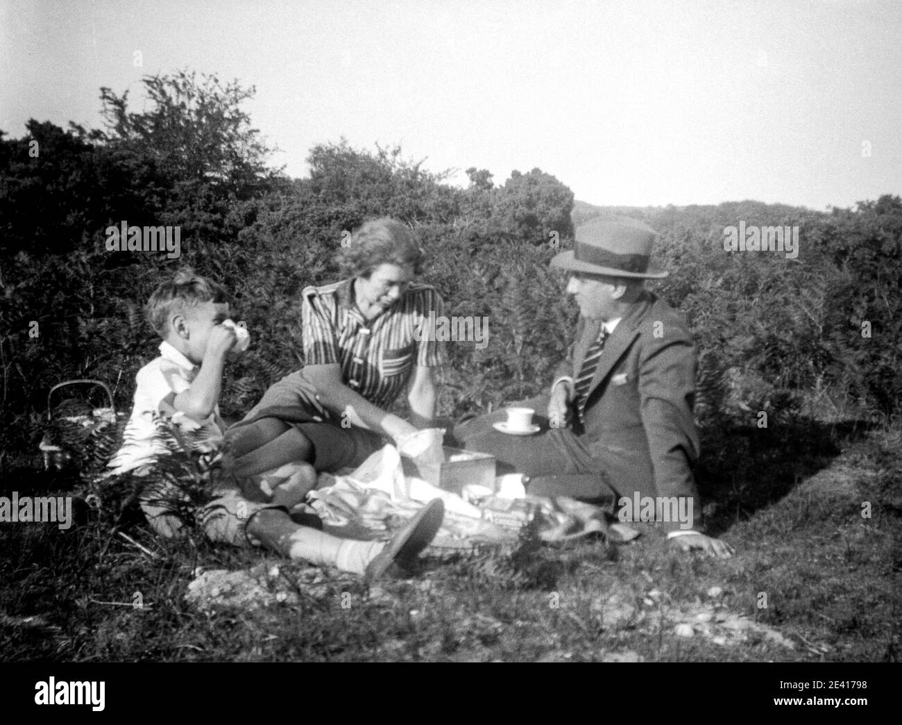 Una madre, un padre y su hijo se sientan felices en el campo haciendo un picnic, disfrutando de la vida al aire libre en la década de 1940 Foto de stock