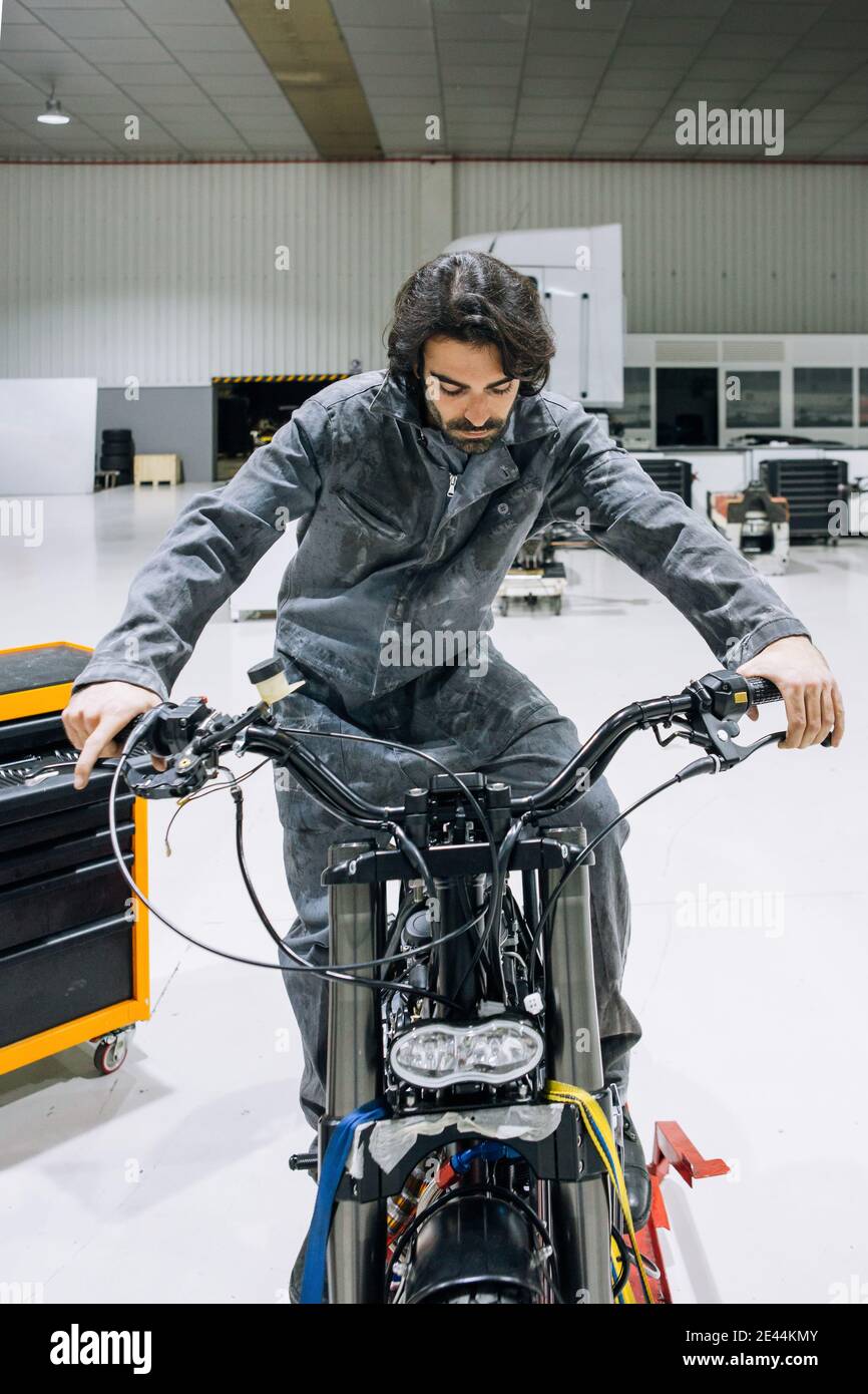 Mecánico masculino experto en ropa de trabajo examinando la moto  personalizada mientras trabaja en el taller moderno profesional Fotografía  de stock - Alamy