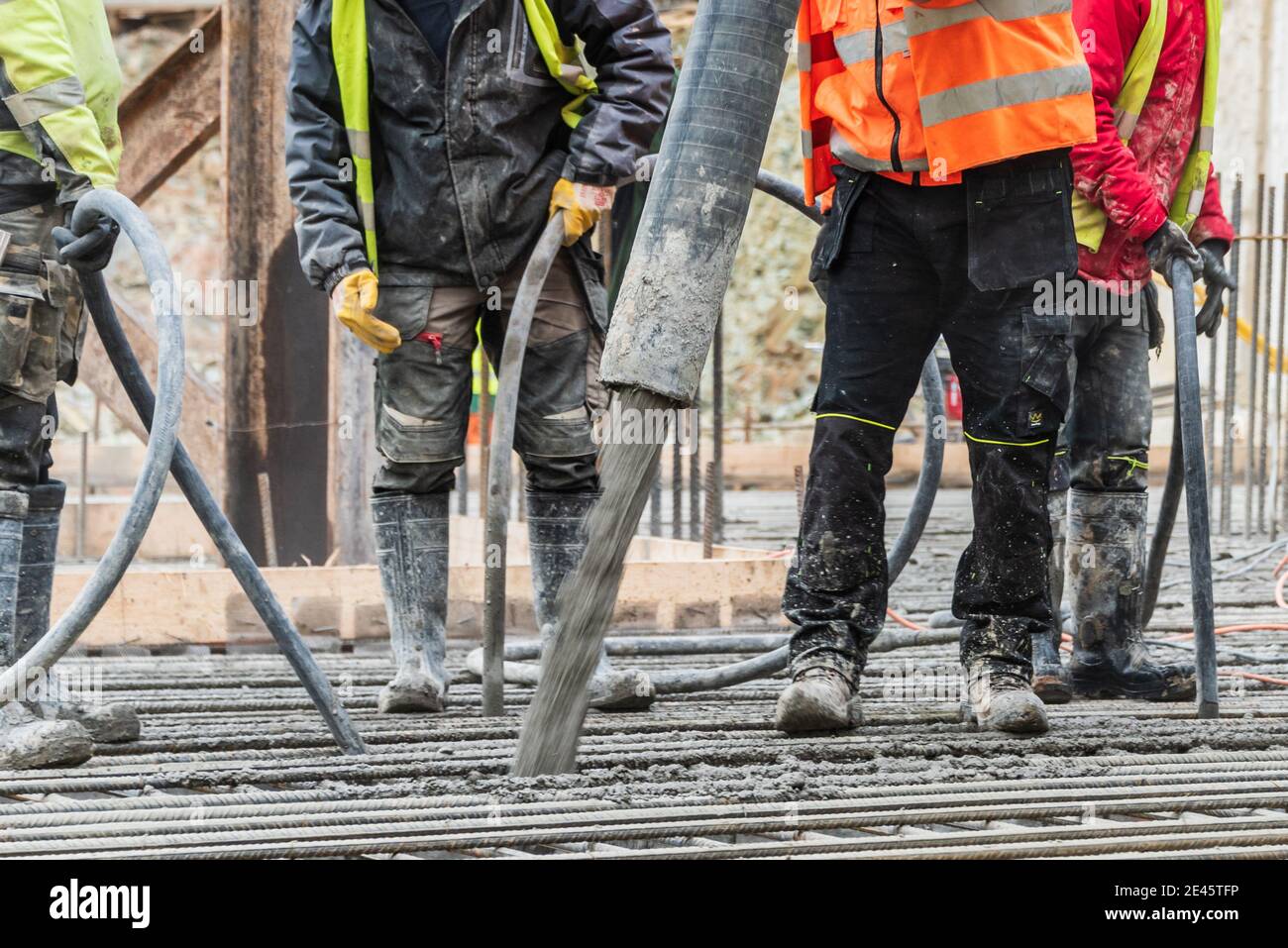 Un grupo de trabajadores de la construcción durante el trabajo de fundición de hormigón, utilizando vibrador de hormigón para compactar hormigón de consistencia rígida. Foto de stock
