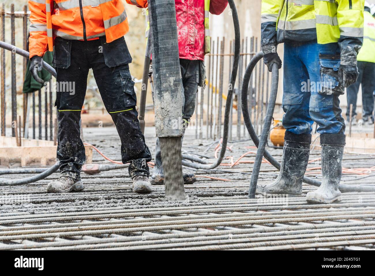 Un grupo de trabajadores de la construcción durante el trabajo de fundición de hormigón, utilizando vibrador de hormigón para compactar hormigón de consistencia rígida. Foto de stock
