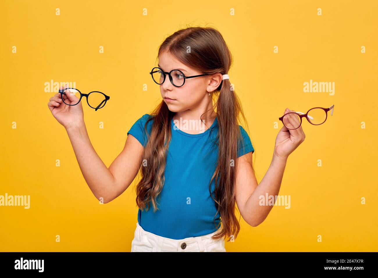 Qué clase de gafas elegir. Chica graciosa con gafas que sostienen gafas con estilo sobre fondo amarillo Foto de stock