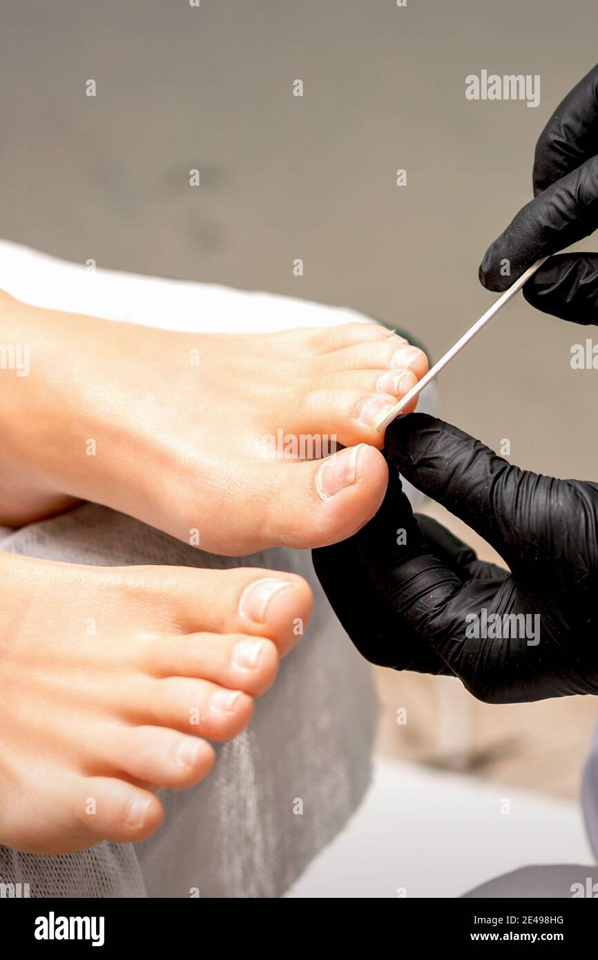 Pedicure las manos del maestro en guantes de goma protectores lime las uñas  de los pies femeninas con un archivo de uñas en un salón de belleza  Fotografía de stock - Alamy