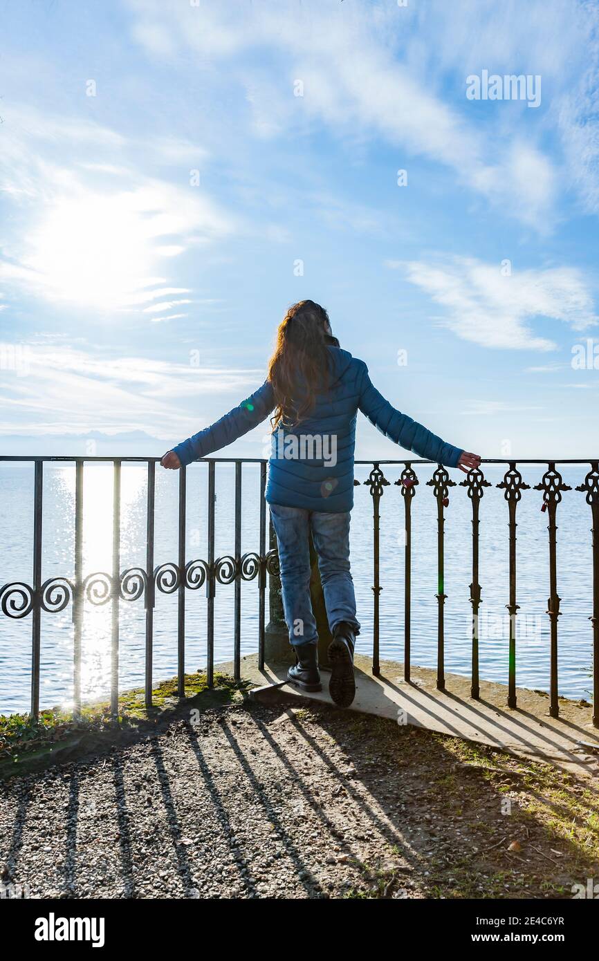 Mujer en una chaqueta de plumón azul en la barandilla un lago Foto de stock