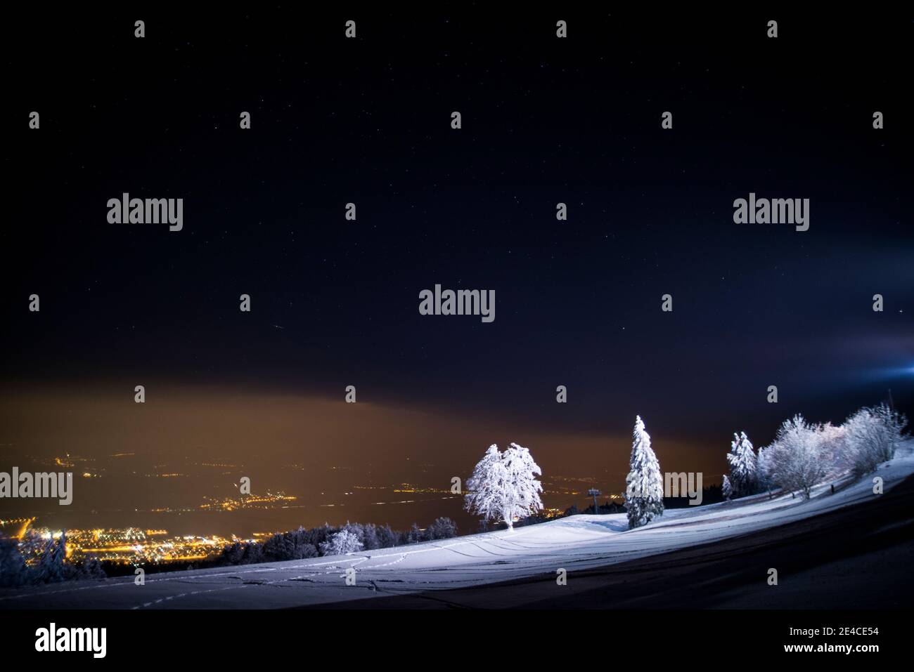 Por la noche, pradera cubierta de nieve en los faros de la estación de montaña, luces en el valle Foto de stock