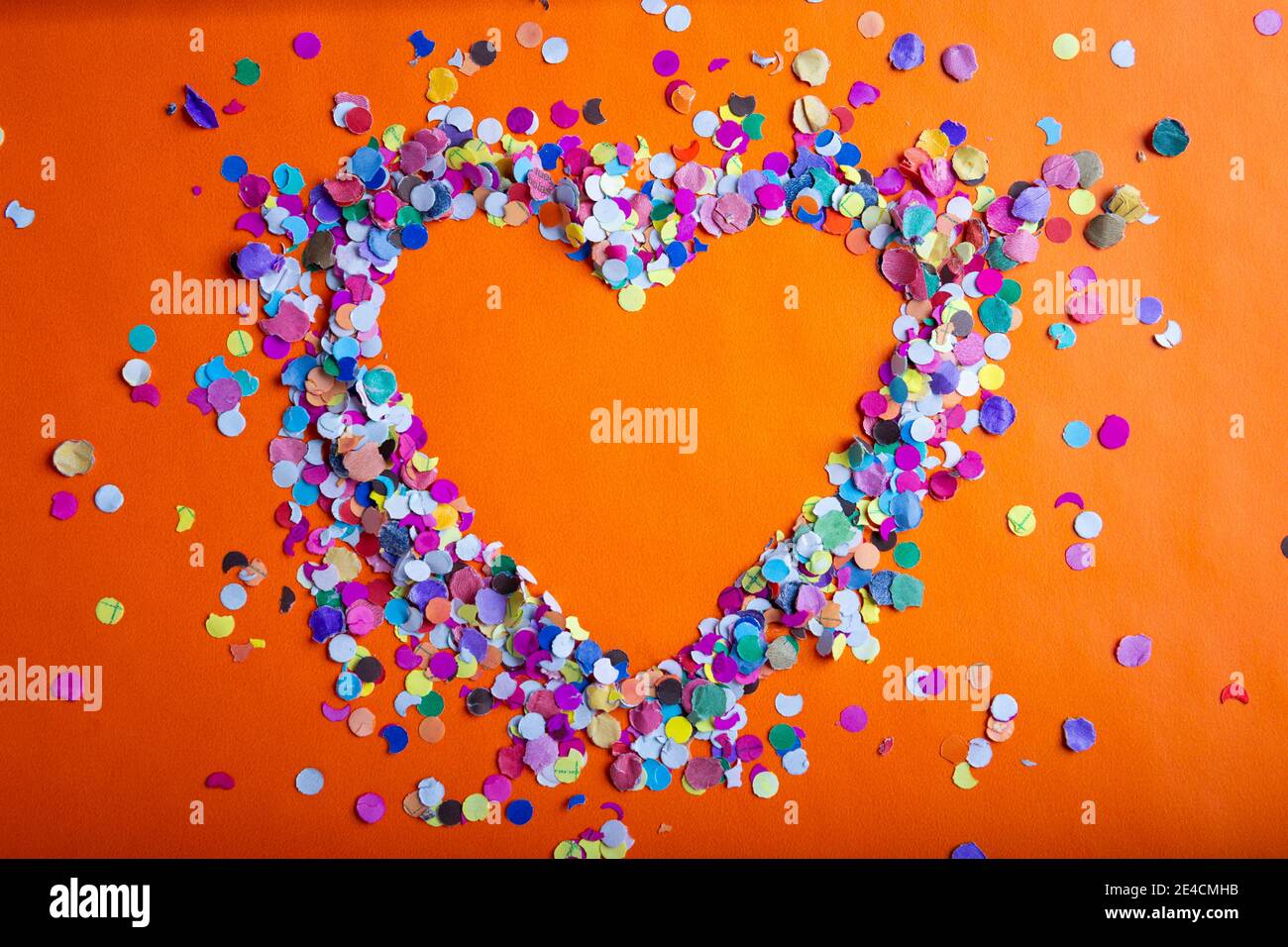 amor concepto imagen de forma de corazón marco hecho de color confeti sobre fondo de textura de papel naranja Foto de stock