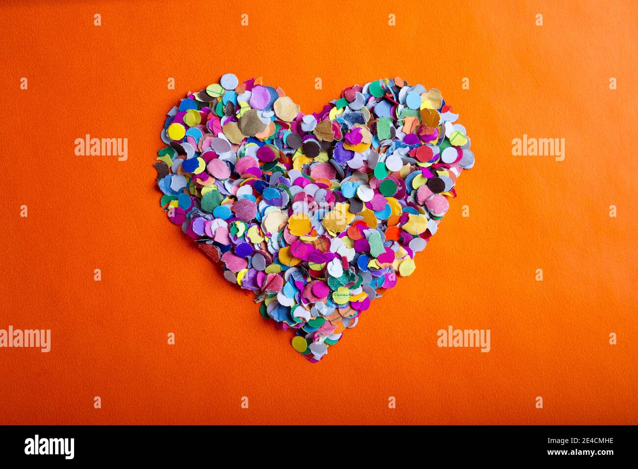 amor concepto imagen de forma de corazón hecho de confeti de colores sobre fondo de textura de papel naranja Foto de stock