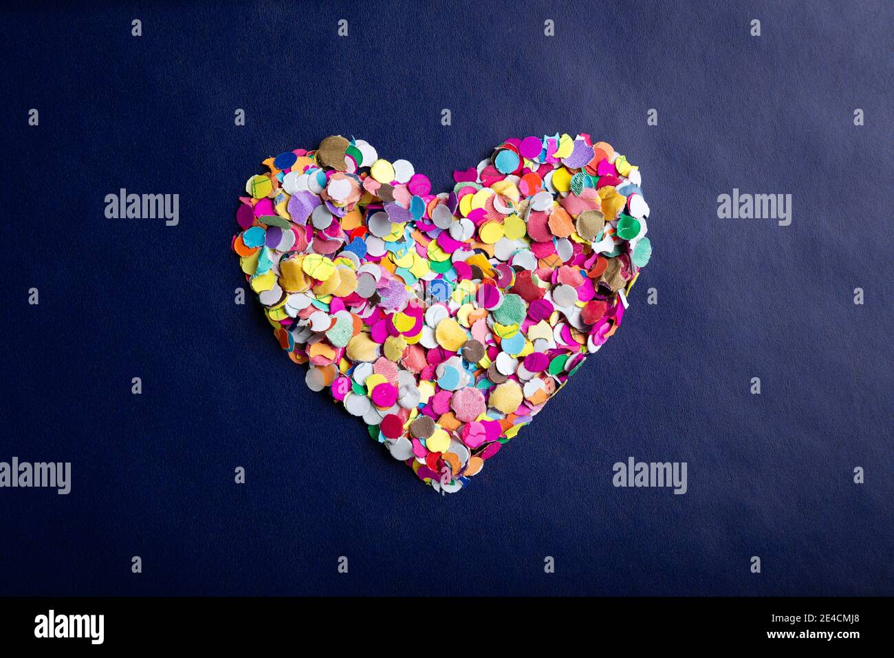 amor concepto imagen de forma de corazón hecho de confeti de colores sobre fondo de textura de papel azul Foto de stock