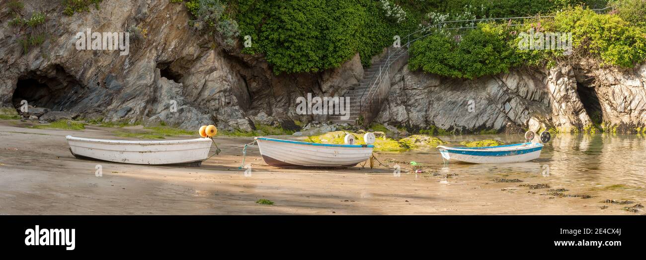 Pequeños botes tirados en una playa con acantilados detrás Foto de stock