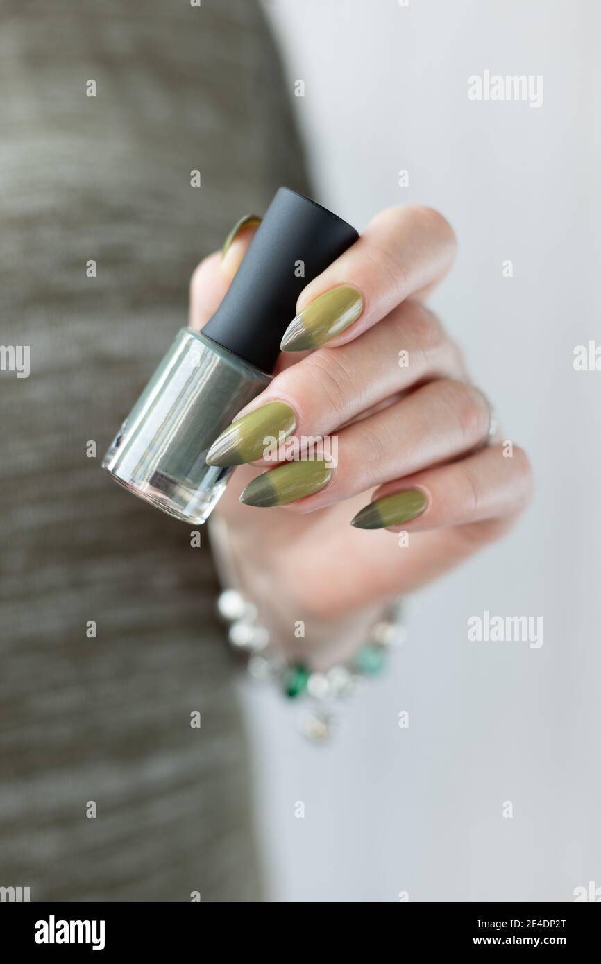 Mano de mujer con uñas largas y manicura verde claro y oscuro con botellas de esmalte de uñas. Foto de stock