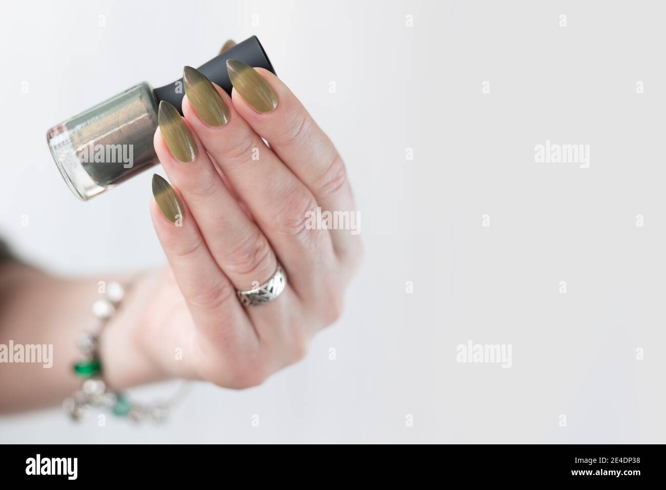 Mano de mujer con uñas largas y manicura verde claro y oscuro con botellas de esmalte de uñas. Foto de stock