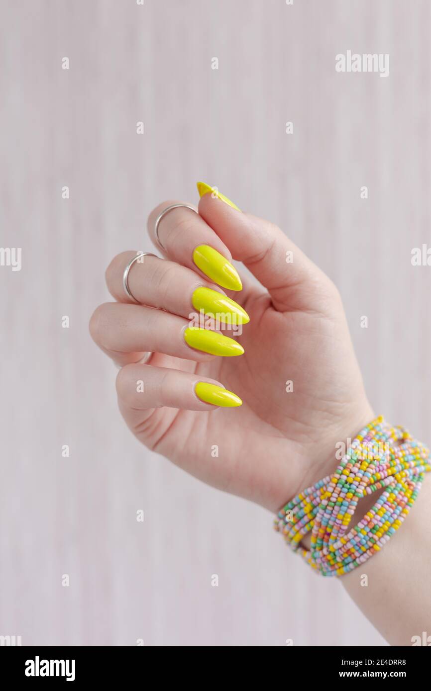 Mano femenina con uñas largas y una botella de brillante esmalte de uñas  amarillo neón Fotografía de stock - Alamy