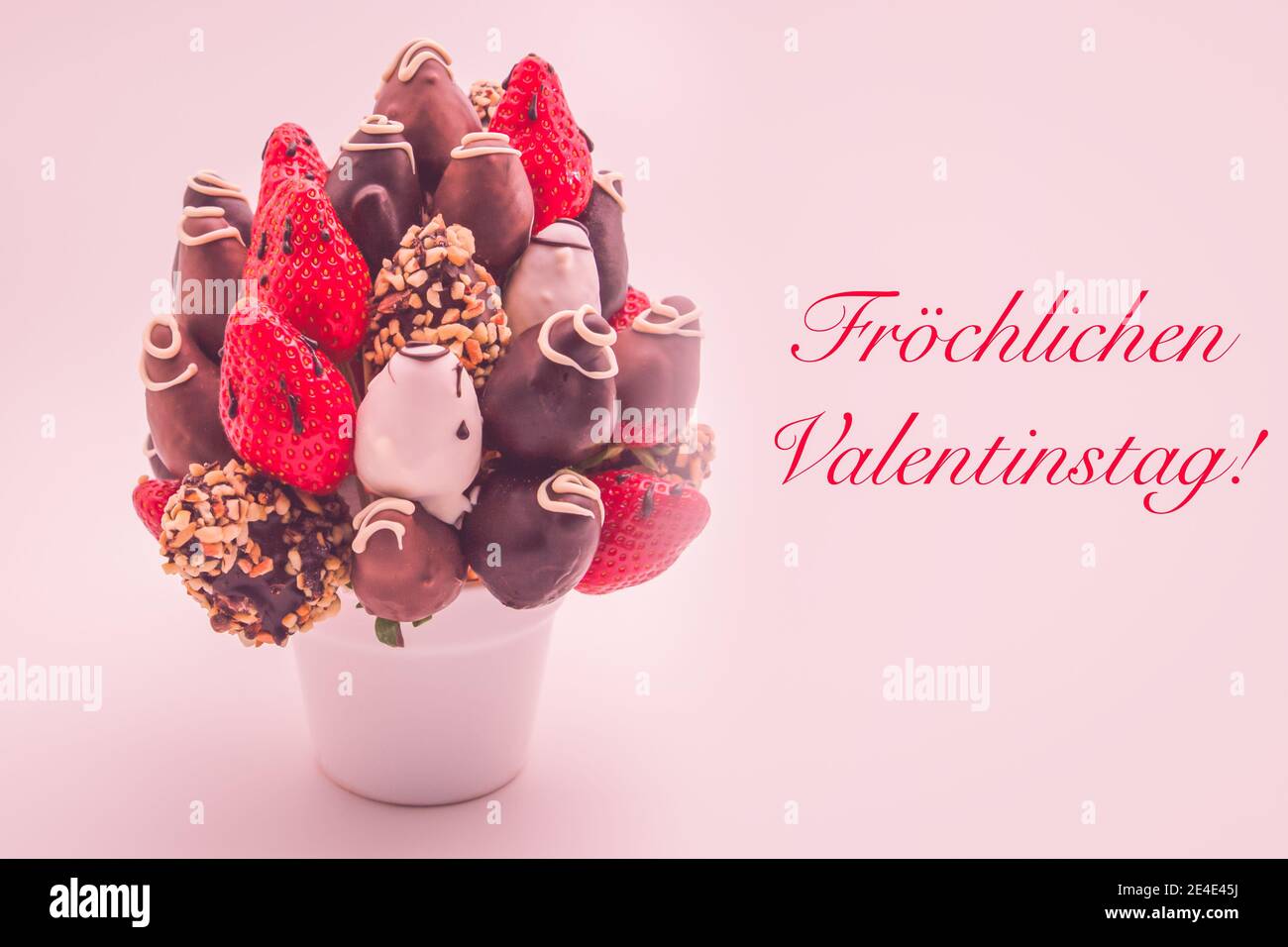 Feliz día de San Valentín tarjeta de felicitación en alemán con letras rojas que dice Fröchlichen Valentinstag; ramo de flores comestibles, arreglo de chocolate Foto de stock