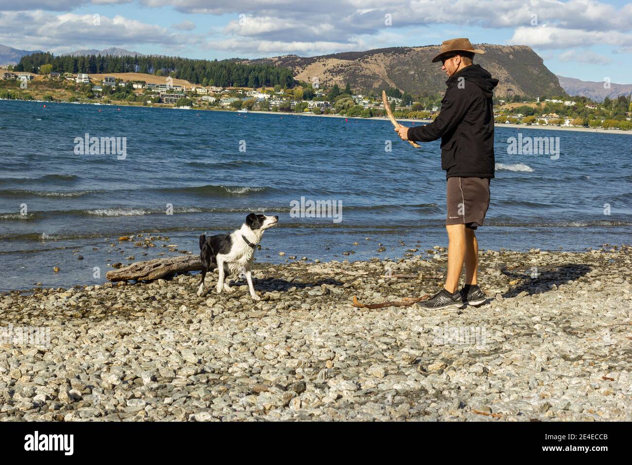 Tiro de un joven con sudaderas con capucha y de pie en la orilla del lago Wanaka con un icónico árbol solitario. Isla Sur de Nueva Zelanda. Foto de stock