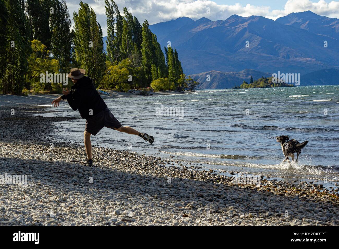 Tiro de un joven con sudaderas con capucha y de pie en la orilla del lago Wanaka con un icónico árbol solitario. Isla Sur de Nueva Zelanda. Foto de stock