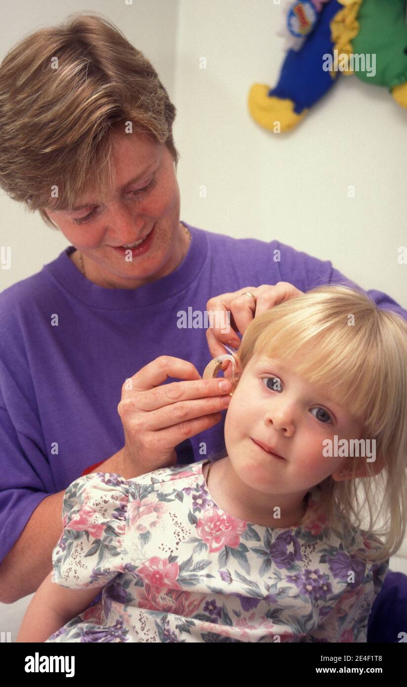 mujer insertando audífonos en el oído de un niño sordo Foto de stock
