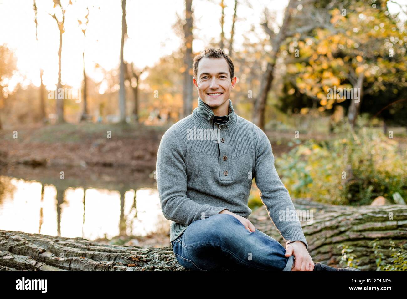 Sonriente hombre medio adulto sentado en el registro en el parque público Foto de stock