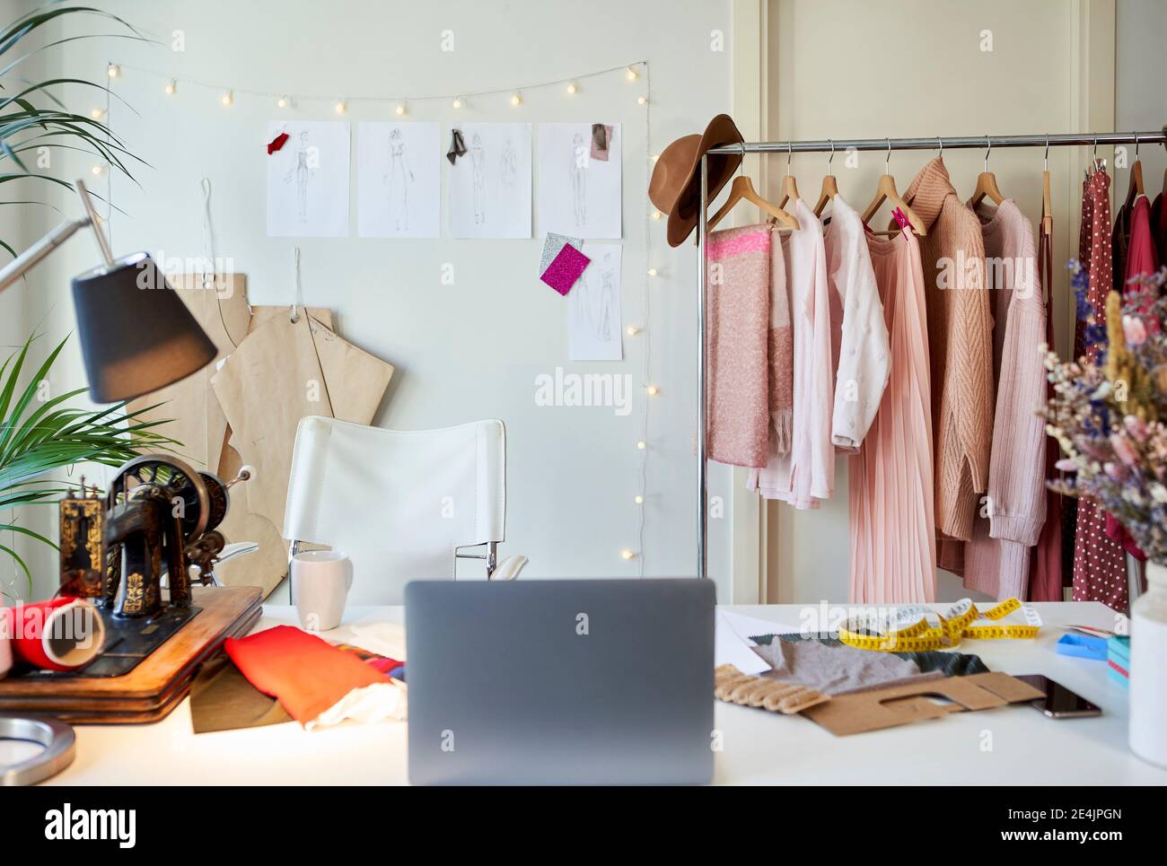 Ordenador portátil en el escritorio junto al estante de ropa en el taller Foto de stock