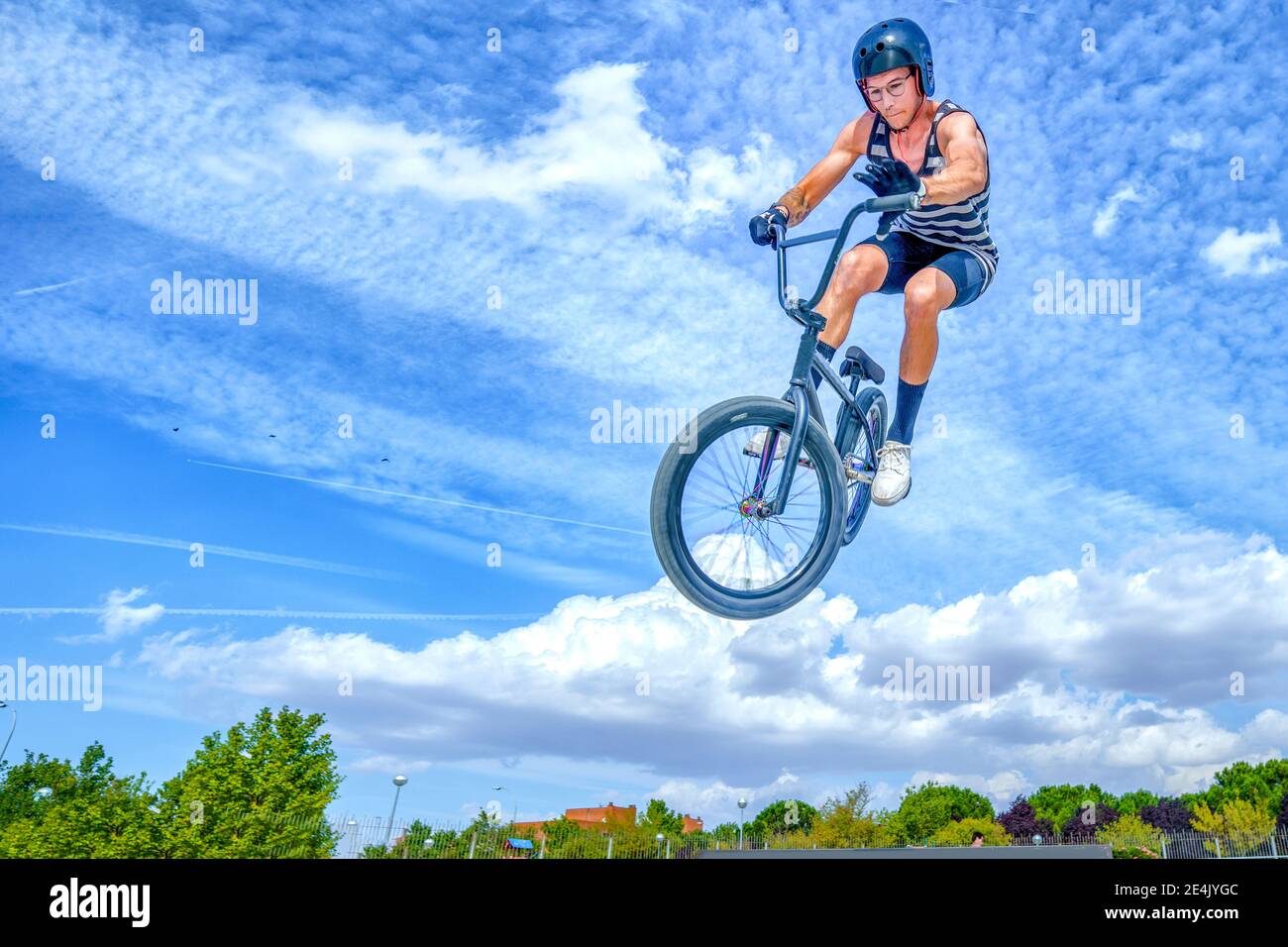 Joven con bicicleta saltando contra el cielo azul en bicicleta parque Foto de stock