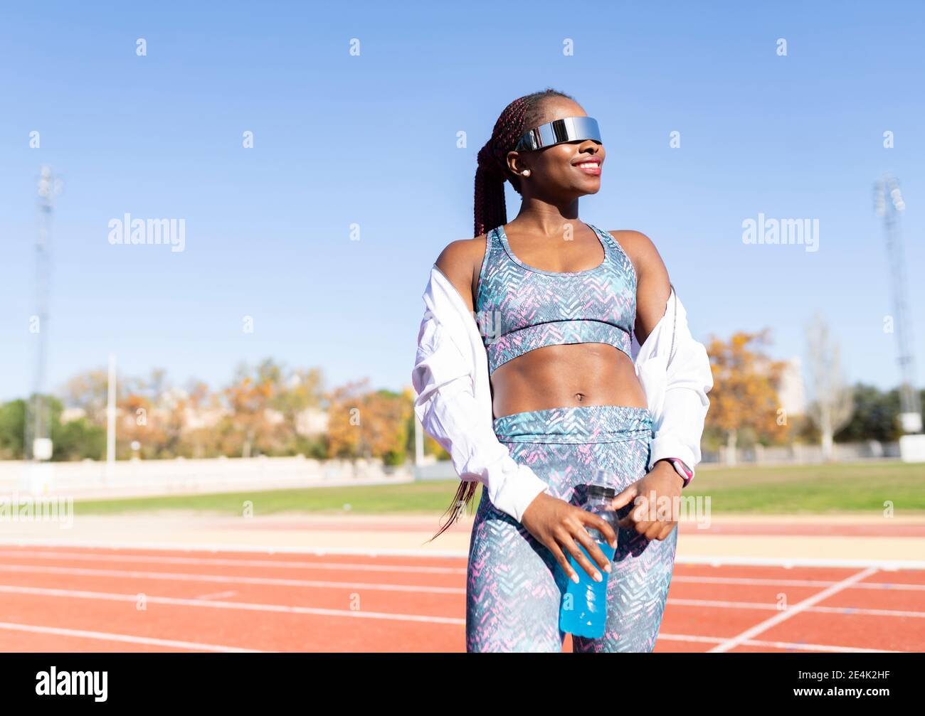 Mujer atleta feliz usando gafas de sol mirando mientras que sostiene la  energía bebe una botella en la pista de deportes Fotografía de stock - Alamy