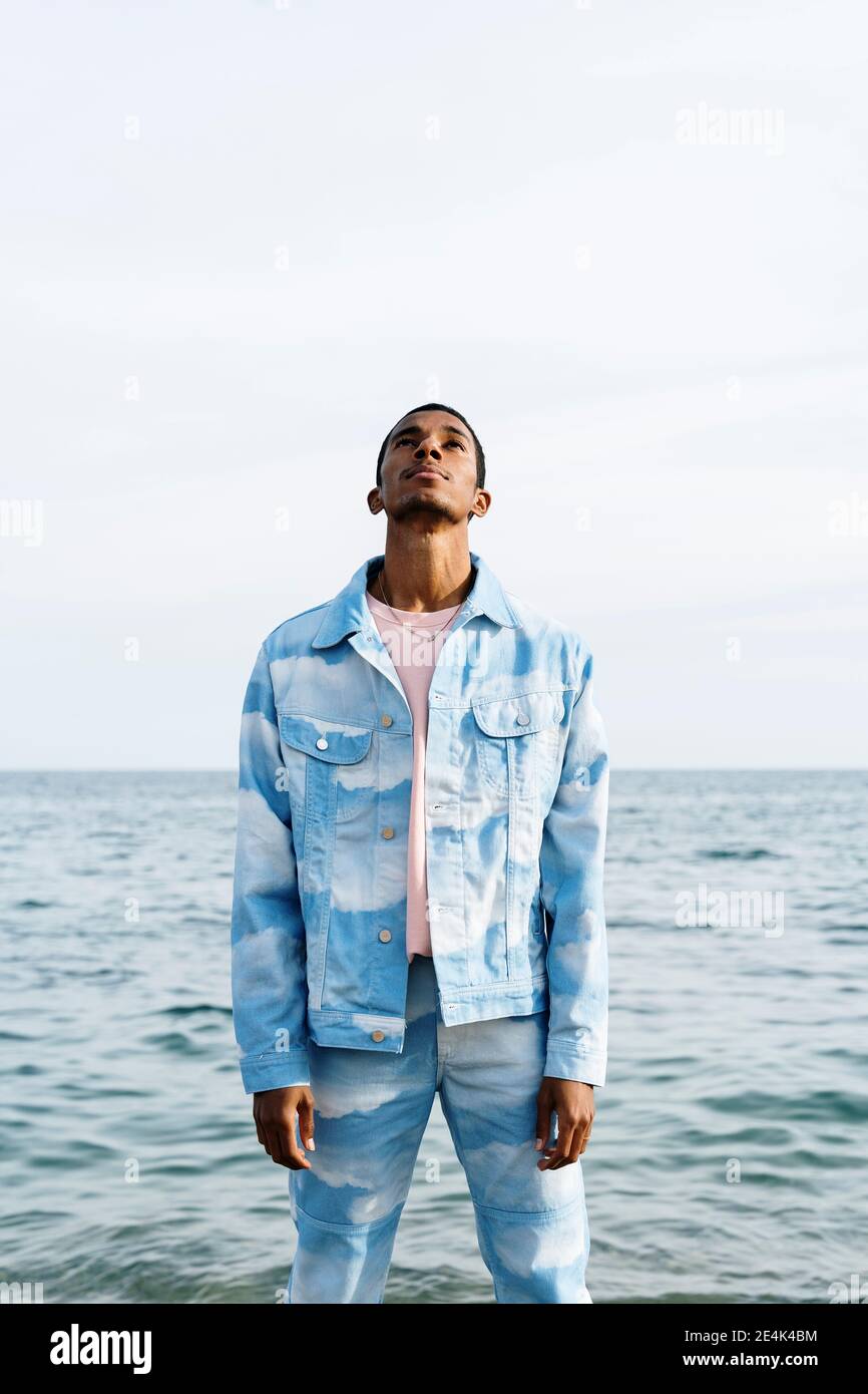 Hombre joven con nubes traje de denim mirando mientras estaba de pie contra  el mar Fotografía de stock - Alamy