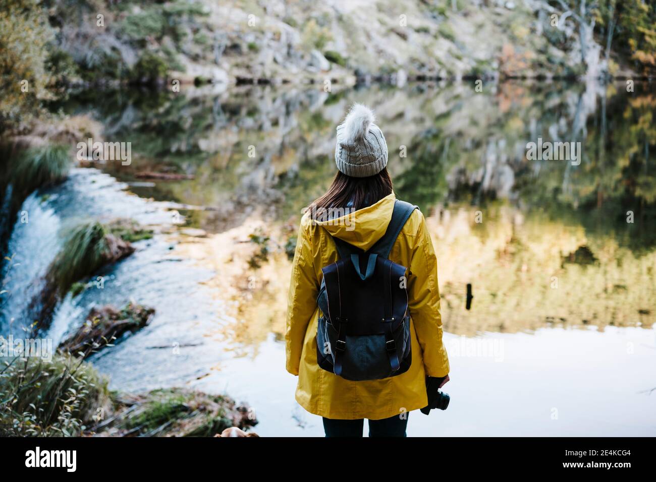 Mujer en chubasquero amarillo frente al río y la cascada Foto de stock