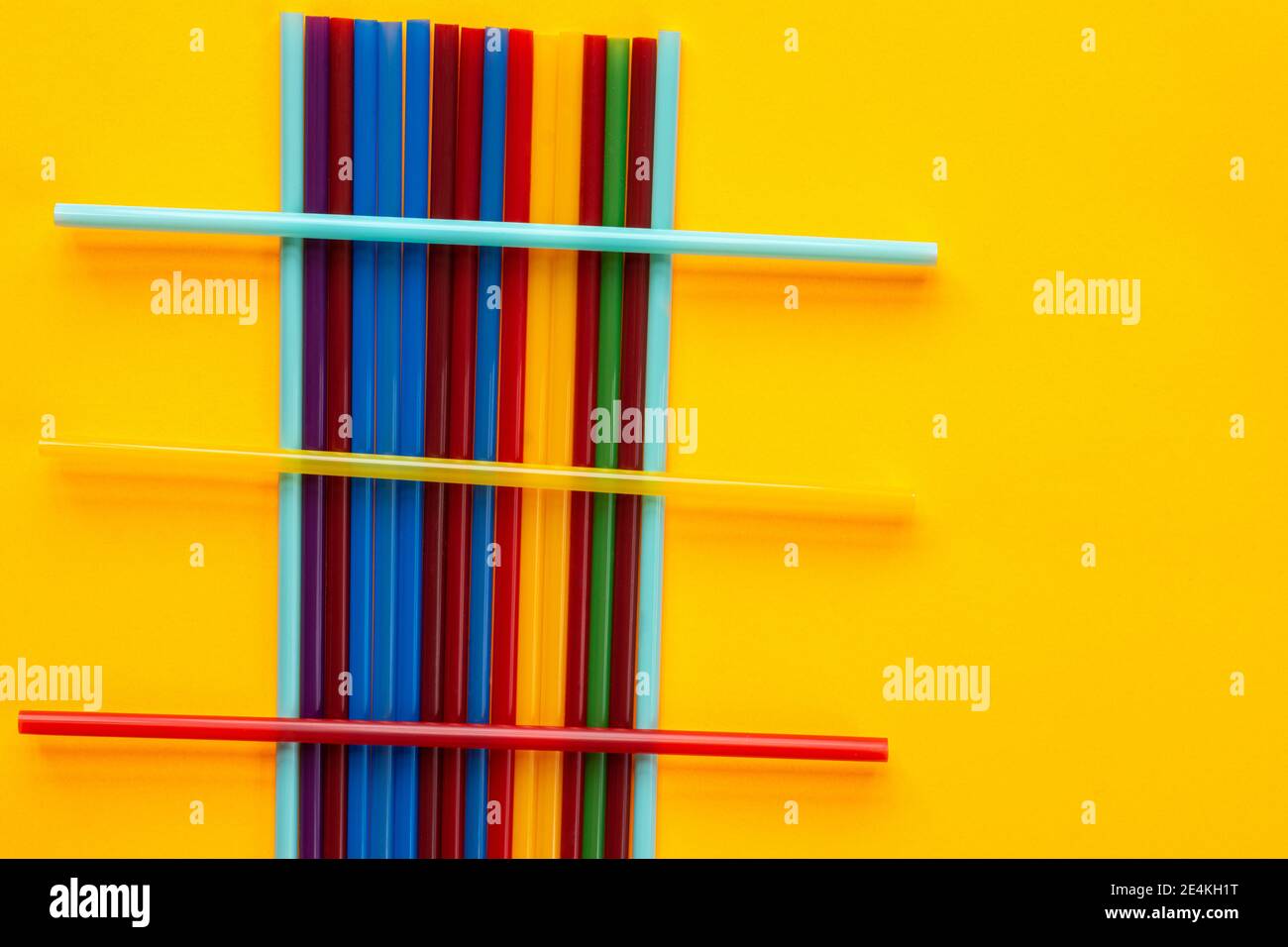 Sobre un fondo amarillo hay tubos de cóctel de varios colores, sobre un montón de tubos verticales son tres horizontales Foto de stock