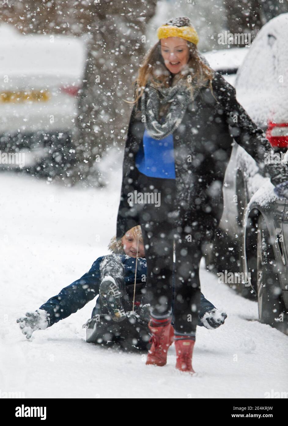 Una madre y su hijo usan un trineo para negociar un camino nevado en Kew, al suroeste de Londres, después de que las pantanosas del Reino Unido se despertaran con nieve y hielo esta mañana, con incluso la capital recibiendo un polvo de blanco. Foto fecha: Domingo 24 de enero de 2021. Foto de stock