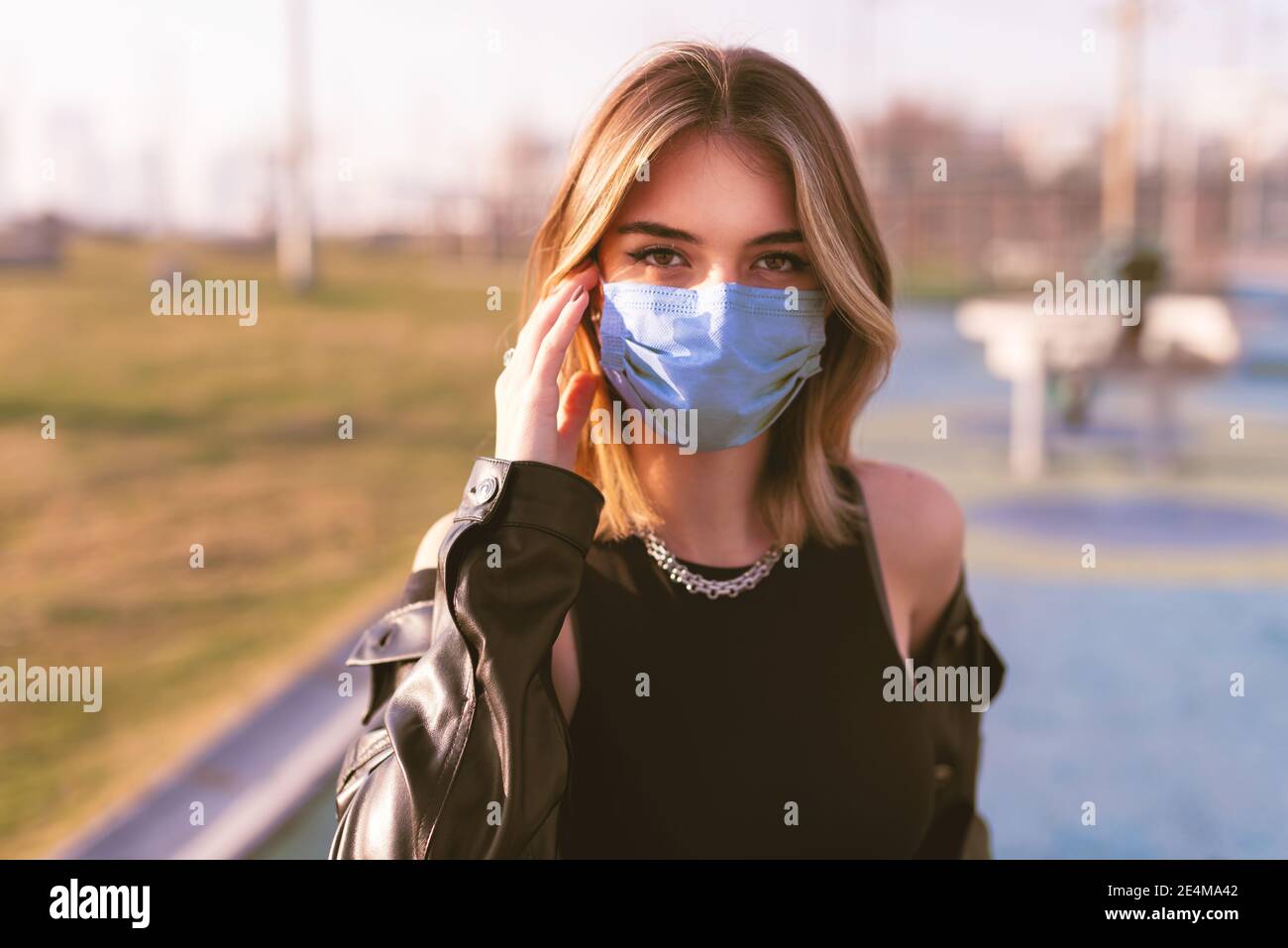 Retrato de una adolescente con una máscara médica en la calle y mirando la cámara. Foto de stock