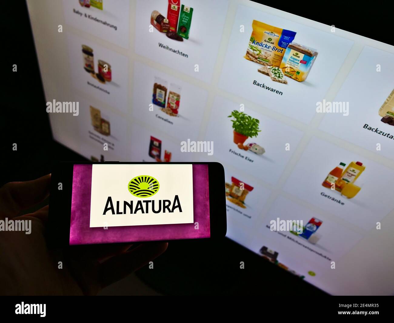 Persona que sostiene el smartphone con el logotipo de la cadena alemana de supermercados de alimentos orgánicos Alnatura Produktions- und Handels GmbH en la pantalla. Enfoque en la pantalla del teléfono. Foto de stock