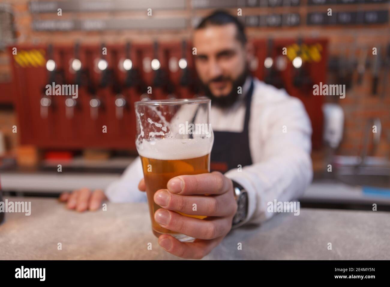 Barman sosteniendo el vaso de cerveza a la cámara, trabajando en su pub Foto de stock