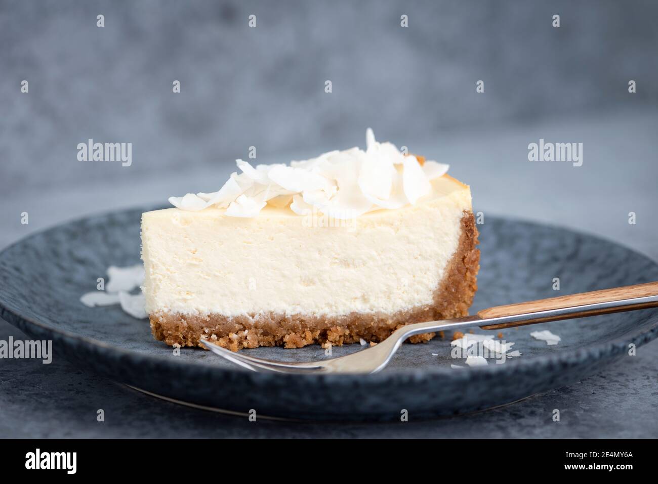 Una rebanada de tarta de queso de coco sobre un plato azul. Deliciosa tarta Foto de stock