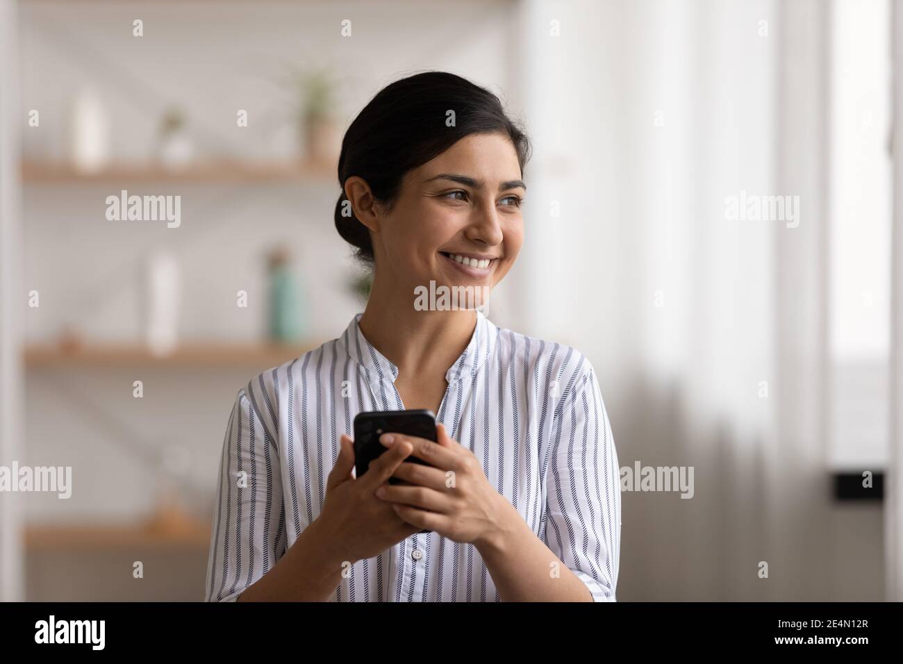 Sonriente de la India de pie con smartphone en la mano mira a un lado Foto de stock