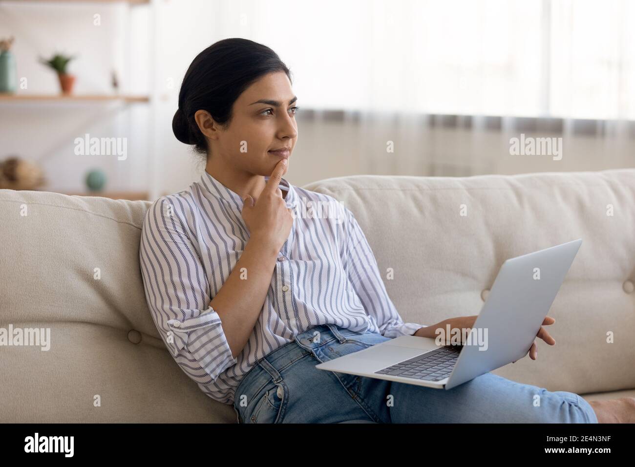 Mujer India mira a un lado de la pantalla del portátil reflexionar sobre el mensaje Foto de stock