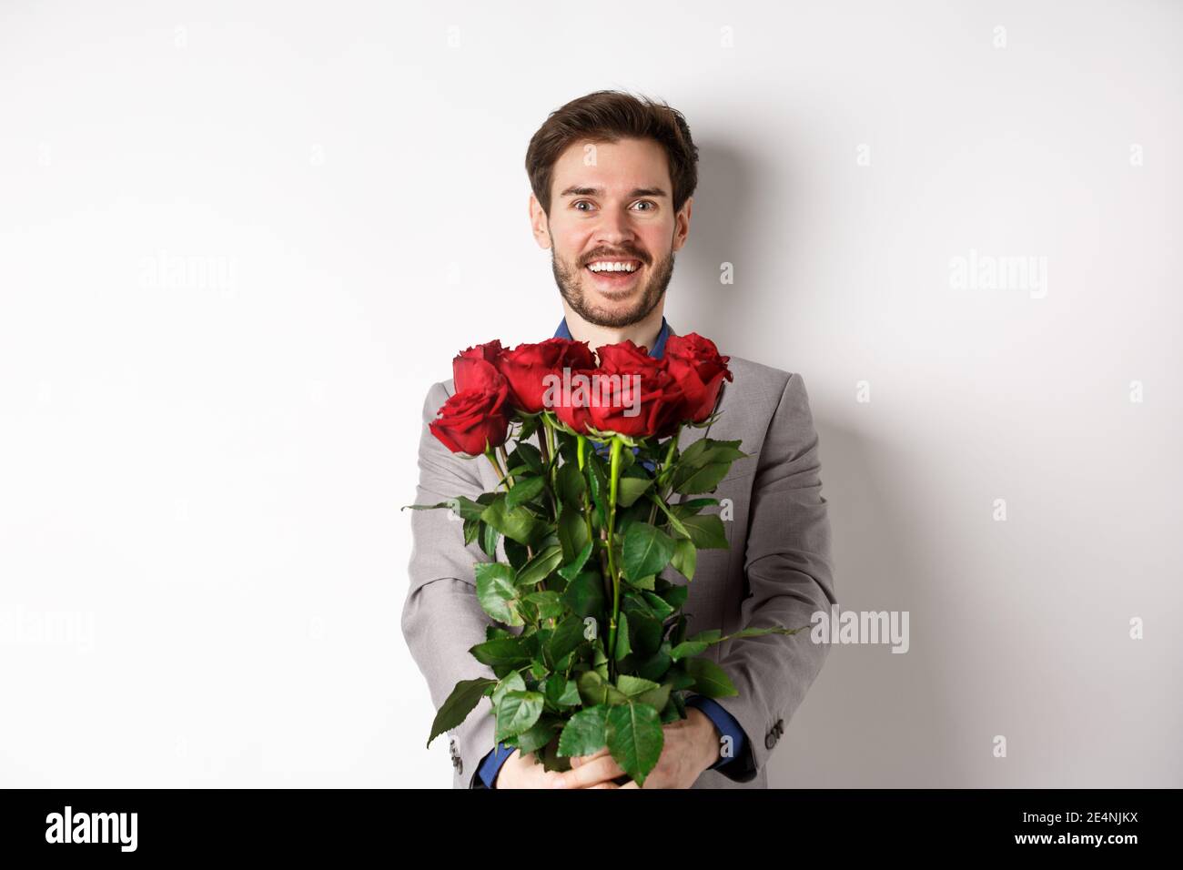 Hombre guapo en el amor deseando feliz día de San Valentín, dando ramo de flores en la cita romántica, sonriendo en la cámara, traje de vestir sobre fondo blanco Fotografía de stock - Hombre guapo en el amor deseando feliz día de San Valentín, dando ramo de flores en la cita romántica, sonriendo en la cámara, traje de vestir sobre fondo blanco Fotografía de stock -