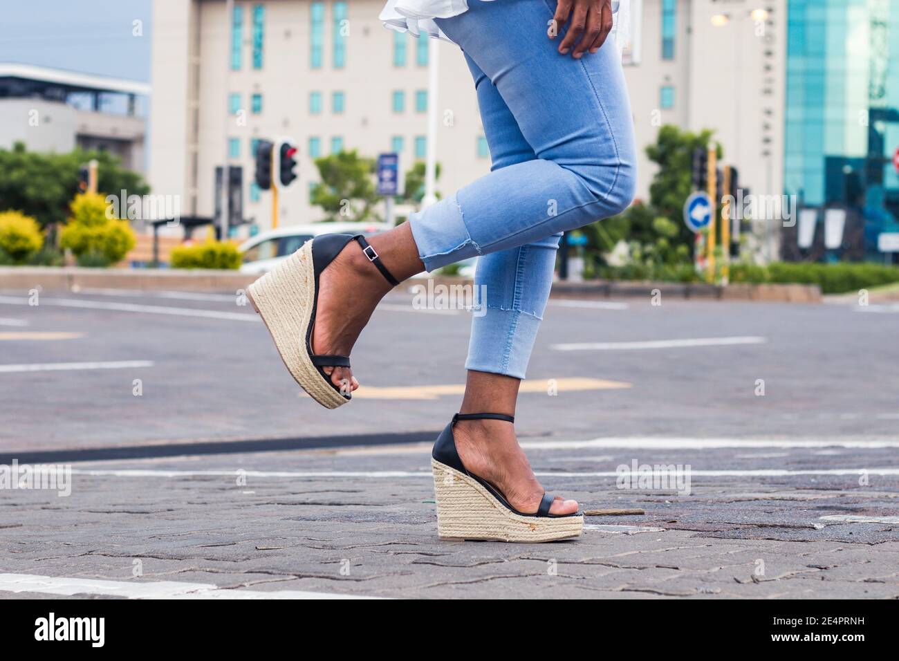 Mujer en azul elegante jeans denim y sandalias cuña con 1 pierna levantada en la calle de la ciudad. Foto de stock