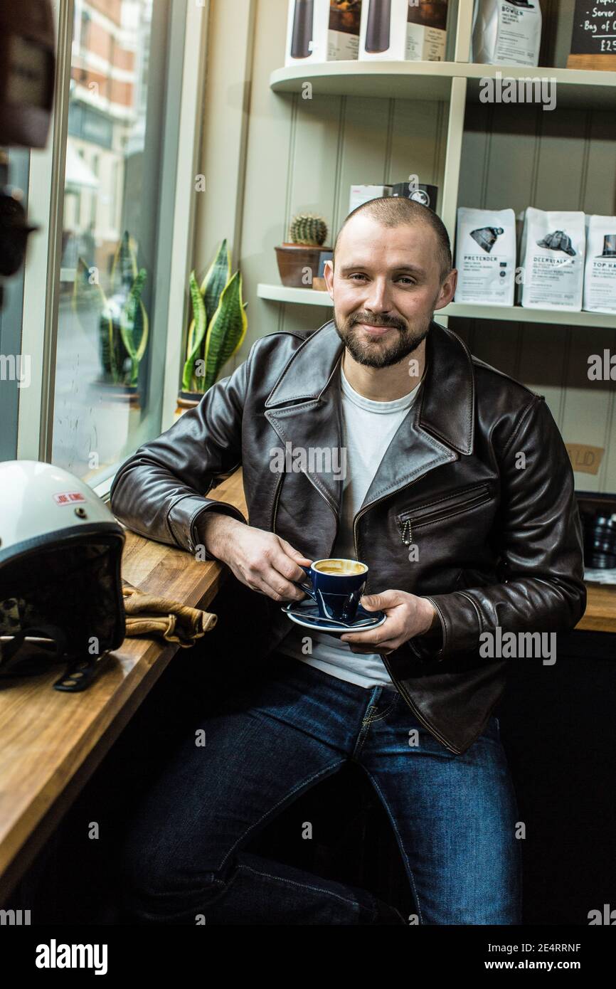 Un hombre toma un descanso para tomar un café en un café de Londres, usando una chaqueta de cuero. Foto de stock