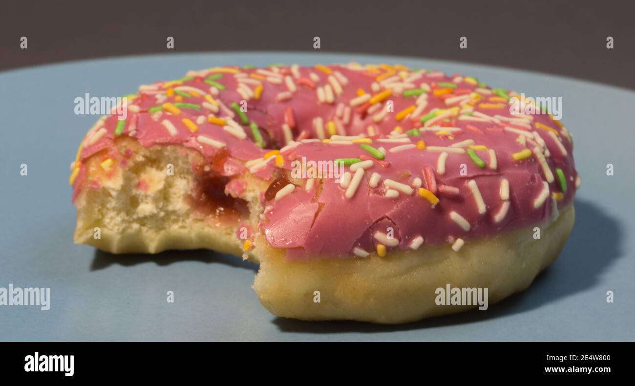 Rosada dulce donut o donut con espolones de color sobre un fondo azul. Mordió el bagel americano. Foto de stock