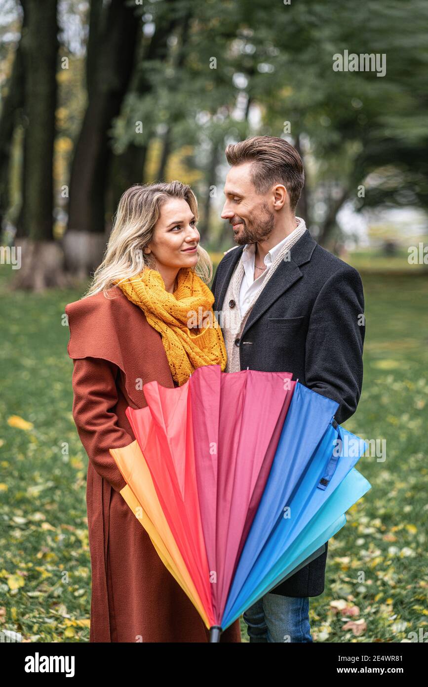 Mirando a los ojos de los demás con el paraguas arco iris cerrado hermoso en pareja de amor de pie en el parque bajo un Una pareja hermosa el otoño Foto de stock