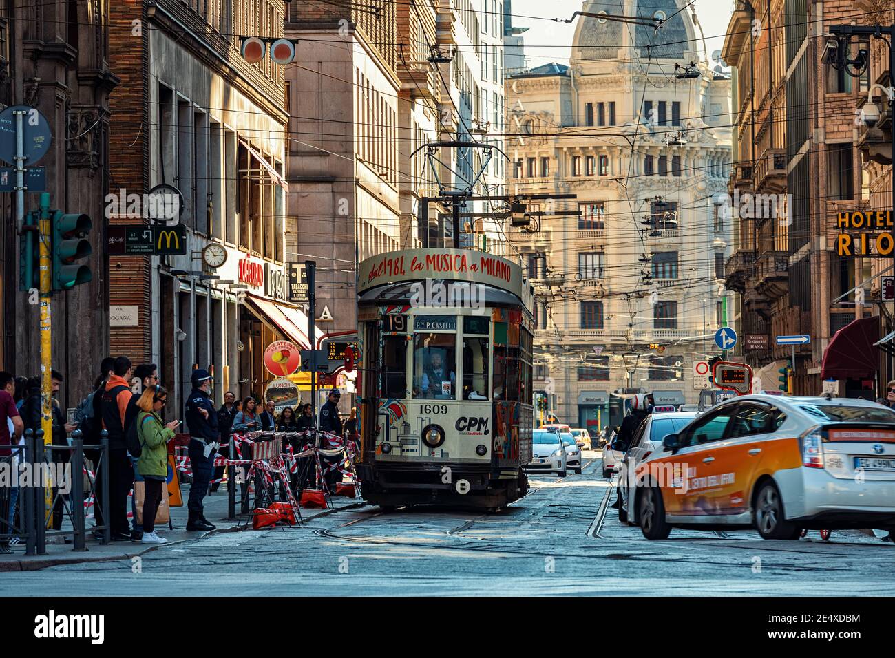 Vista típica de la calle con la gente y la carretera de la ciudad con los coches y el antiguo tranvía histórico en Milán, Italia. Foto de stock