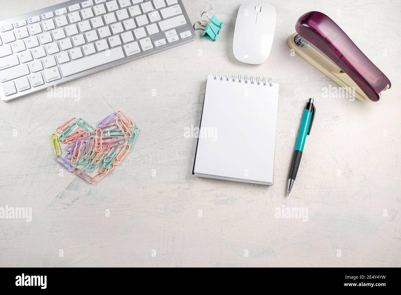 Clips de papel de color en forma de corazón en un escritorio con un bloc de notas en blanco para escribir. Día de San Valentín en la oficina. Vista superior Foto de stock