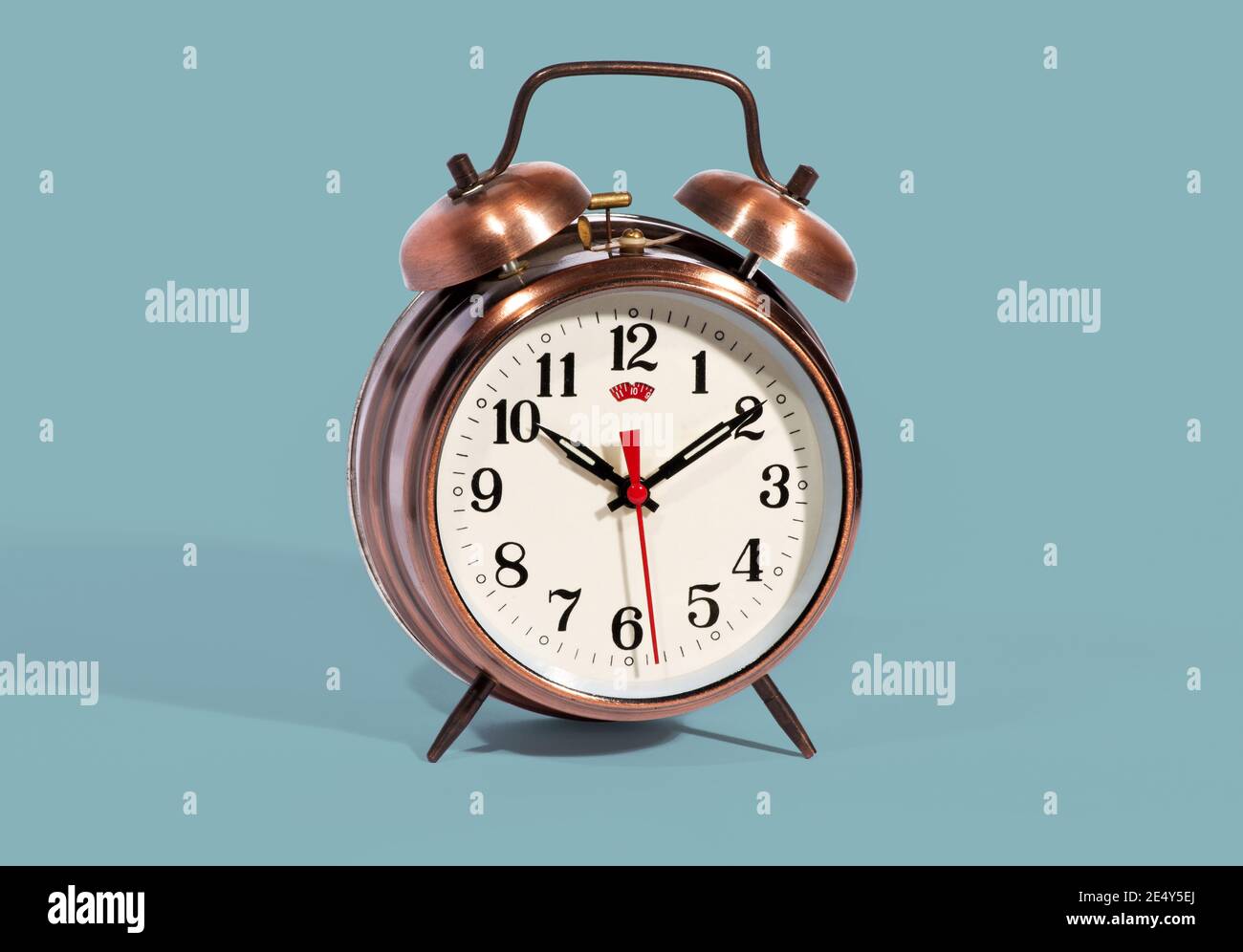 Reloj de alarma clásico de color bronce estilo vintage con campanas y. un dial moderno con una segunda mano roja en un fondo azul Foto de stock