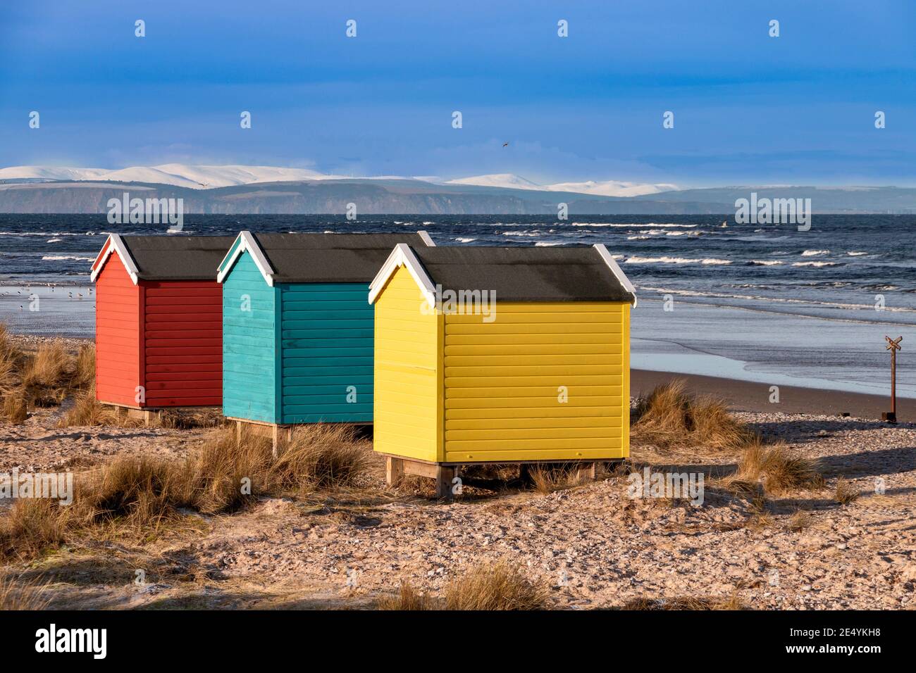 FINDHORN MORAY COSTA ESCOCIA LA PLAYA CON CHALETS DE COLORES O. CABAÑAS EN INVIERNO MONTAÑAS CUBIERTAS DE NIEVE MÁS ALLÁ Foto de stock