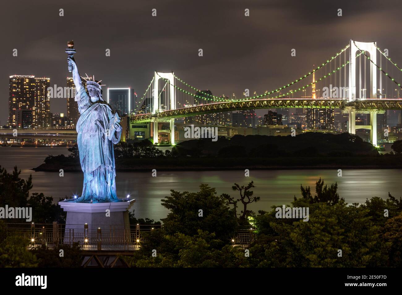 El horizonte de Tokio por la noche visto desde Odaiba, con un puente colgante una estatua de la libertad réplica Foto de stock