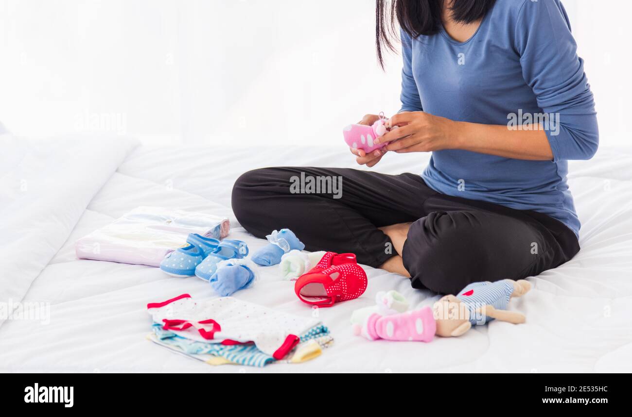 Madre asiática preparando la ropa del bebé descansando y relajándose en el cama hace comprar ropa para después del bebé preparándose para el nacimiento del recién nacido Fotografía de stock -