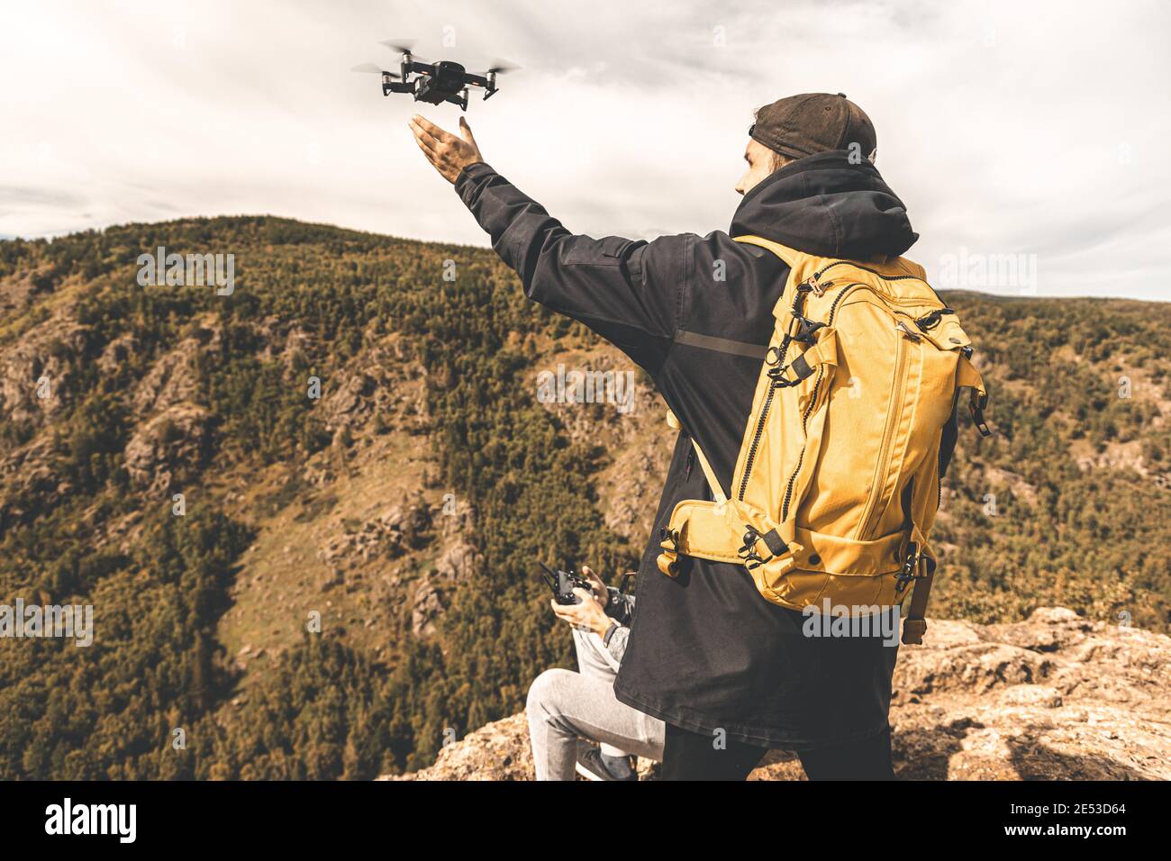 Un hombre con una mochila amarilla va de excursión entre el montañas y  lanza un drone Fotografía de stock - Alamy