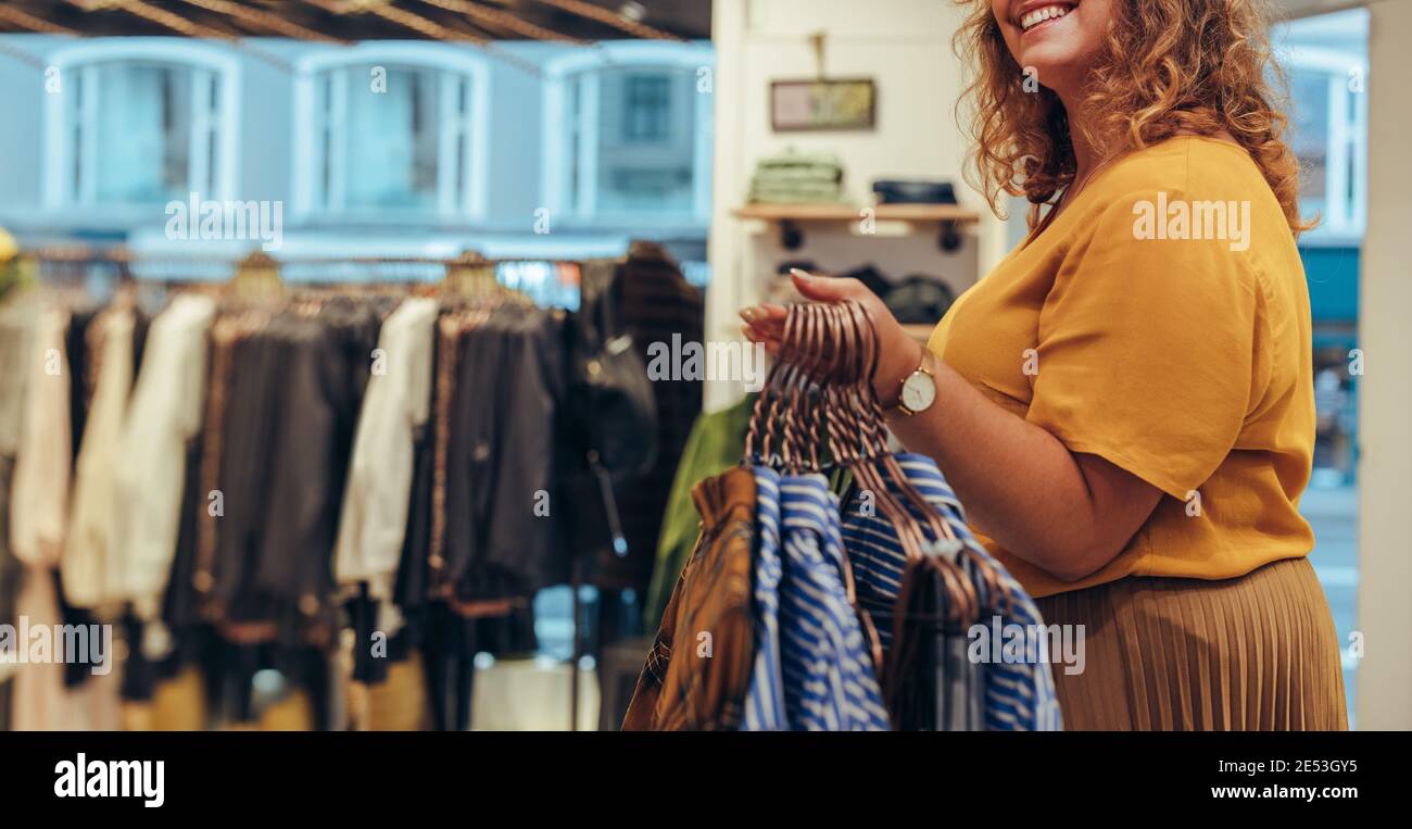 Propietario de la tienda de moda llevando ropa en perchas para organizar en la vichera. Tiro recortado de una mujer que trabaja en tienda de ropa, ropa colgada Foto de stock