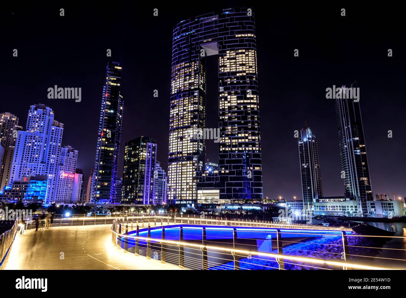 Hermosa vista nocturna de los rascacielos iluminados en el dubai puerto deportivo capturado desde el puente del muelle que conecta Ain Dubai en islas de agua azul Foto de stock